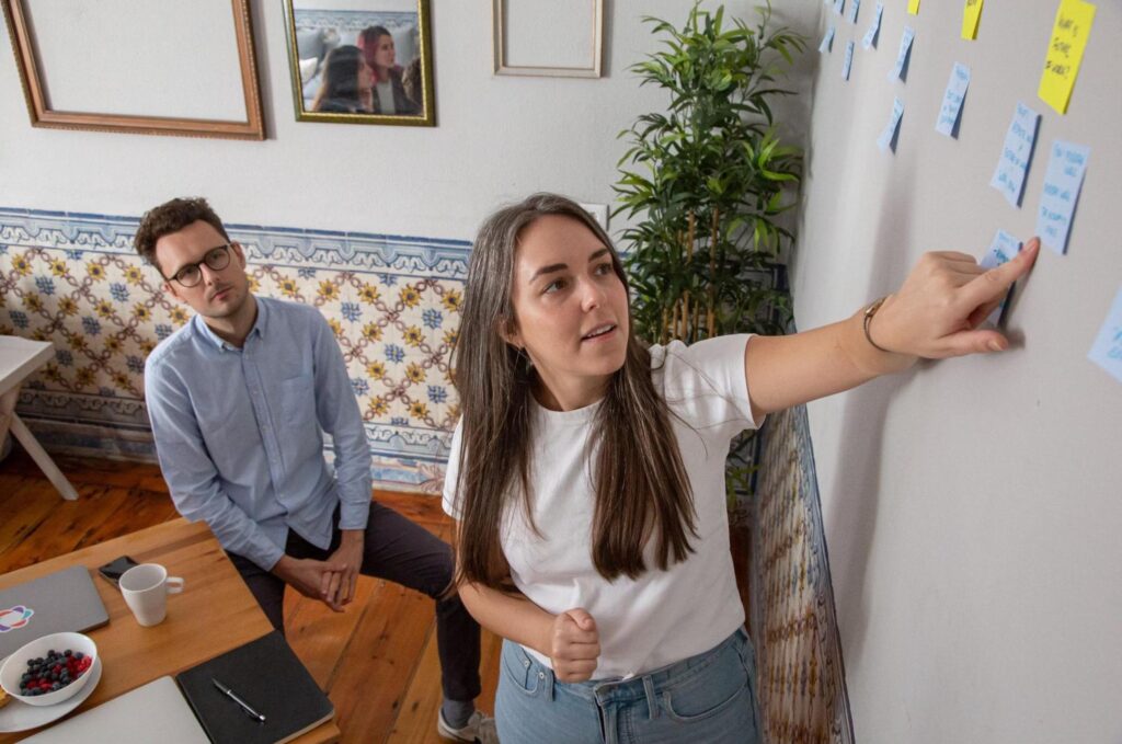 A girl showing her colleague a post it on the wall