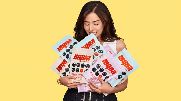 influencer Pokimane holding her new product Myna Snacks in front of a yellow background