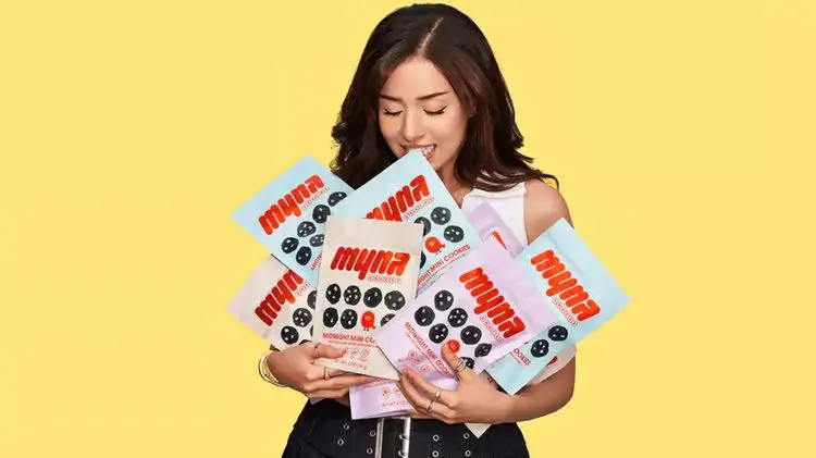 influencer Pokimane holding her new product Myna Snacks in front of a yellow background