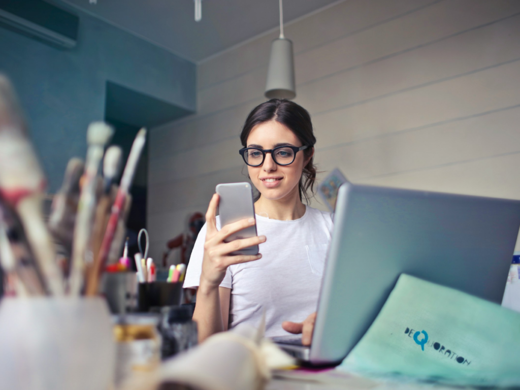 Woman holding phone looking at laptop in office setting