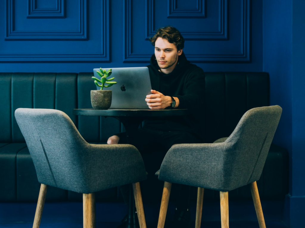 Man sitting in chair working on laptop in front of blue background